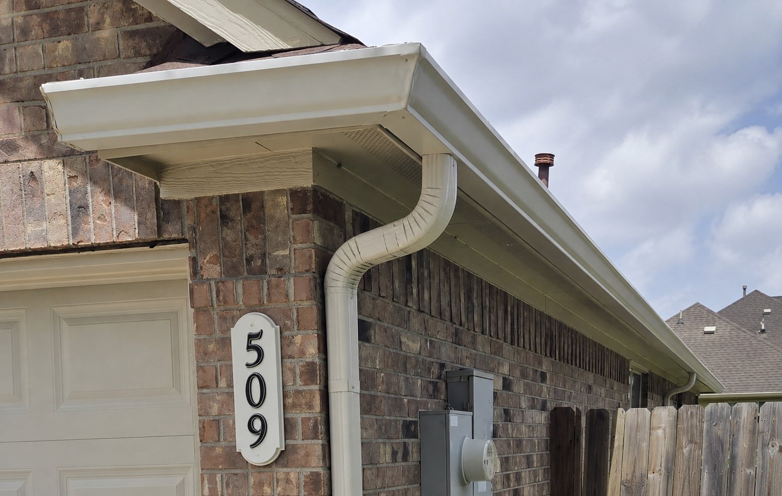 Cream seamless gutter and downspout installed along a brick home in Mission, Texas