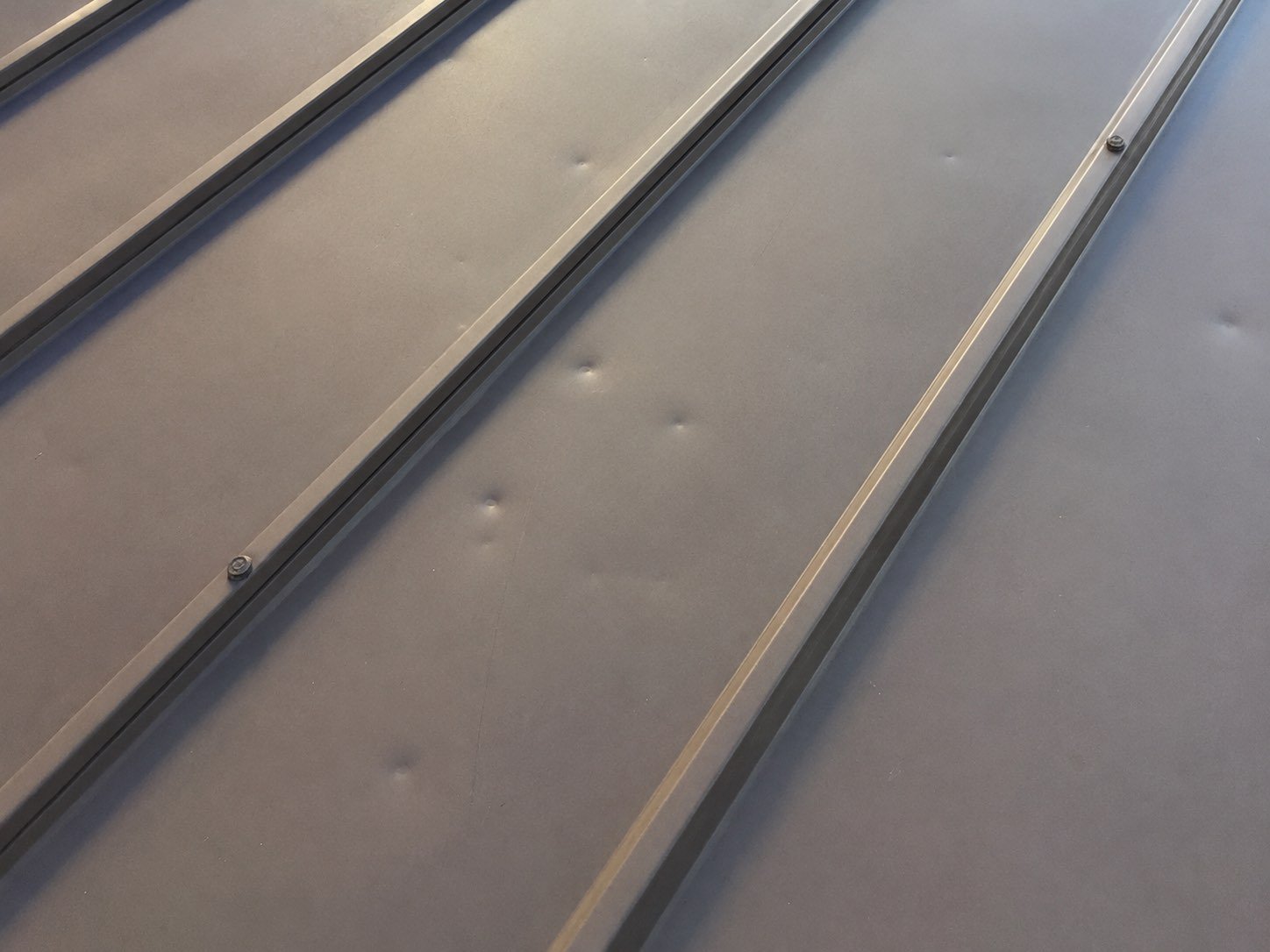 Hail dents across standing seam metal roof panels in Edinburg, Texas showing cosmetic denting between the seams